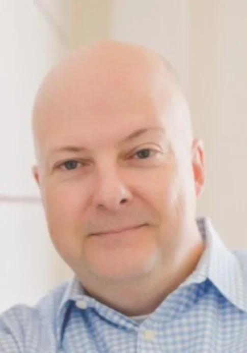 Smiling man in a blue checkered shirt.